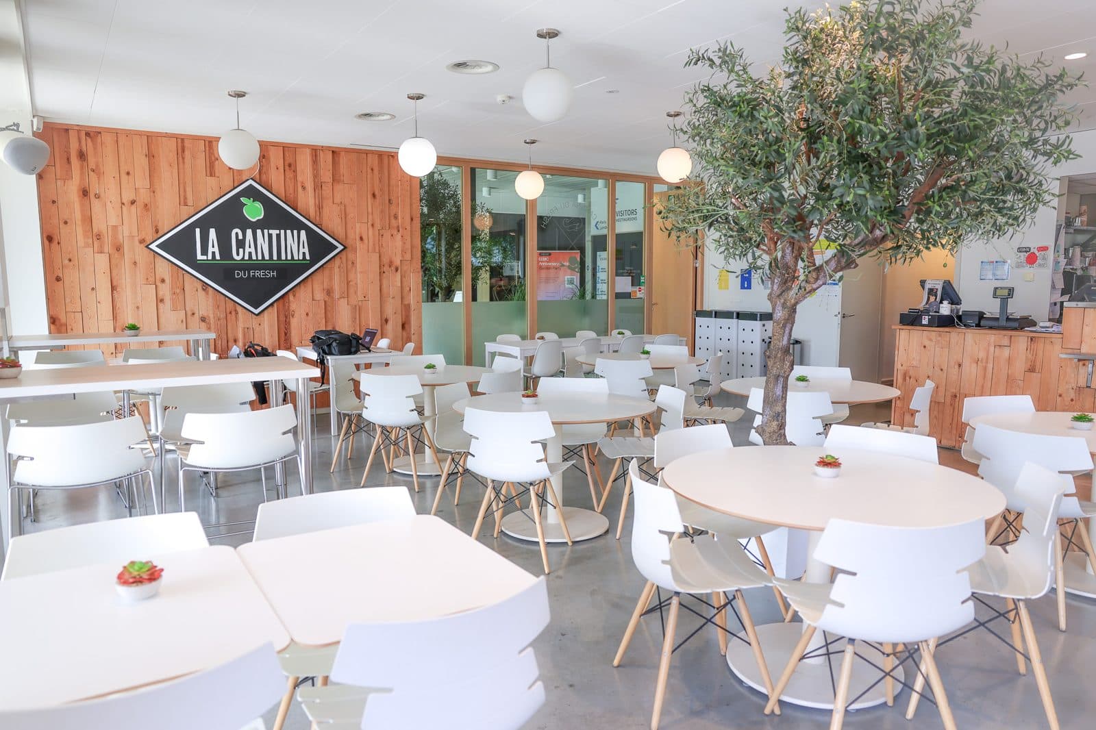 Salle de la cantine : tables blanches, olivier et logo diamant au mur